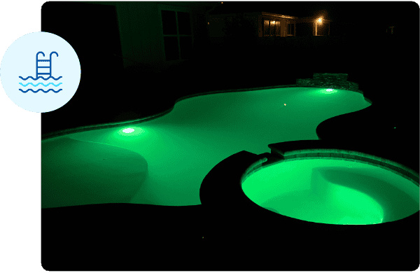 Custom pool shape with spa lit up at night with green lights.